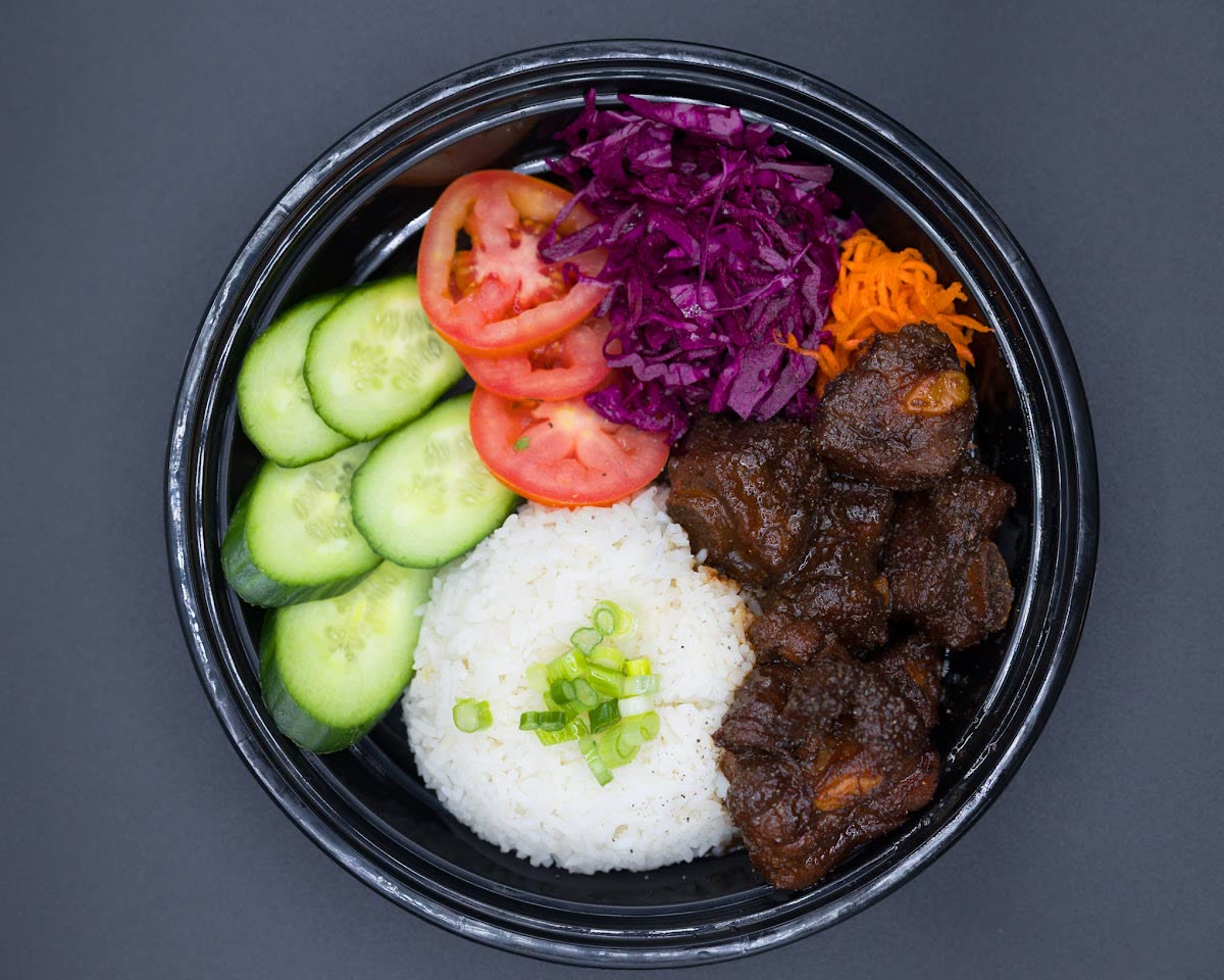 Overhead view of a rice bowl with grilled meat, cucumber, tomato, and shredded cabbage