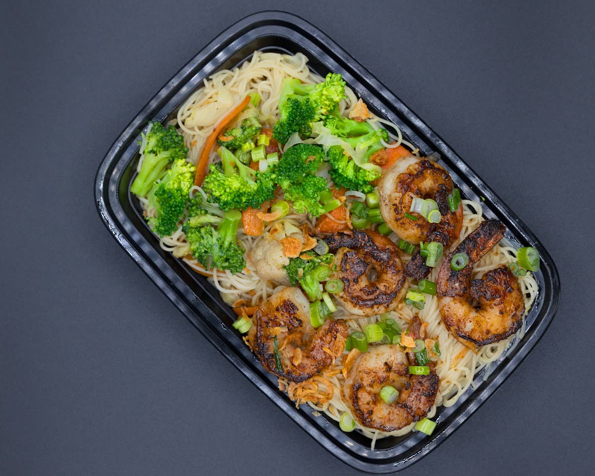 Overhead view of shrimp, noodles, and green vegetables in a takeaway tray